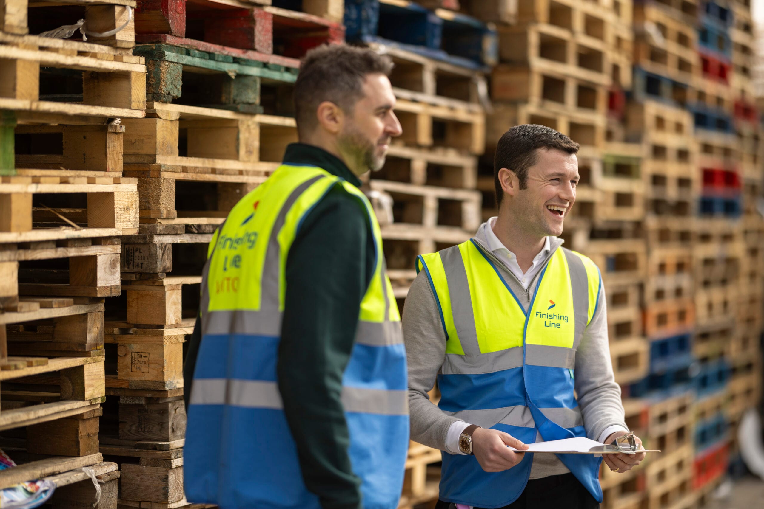 Picture of two staff members in front of a stack of pallets